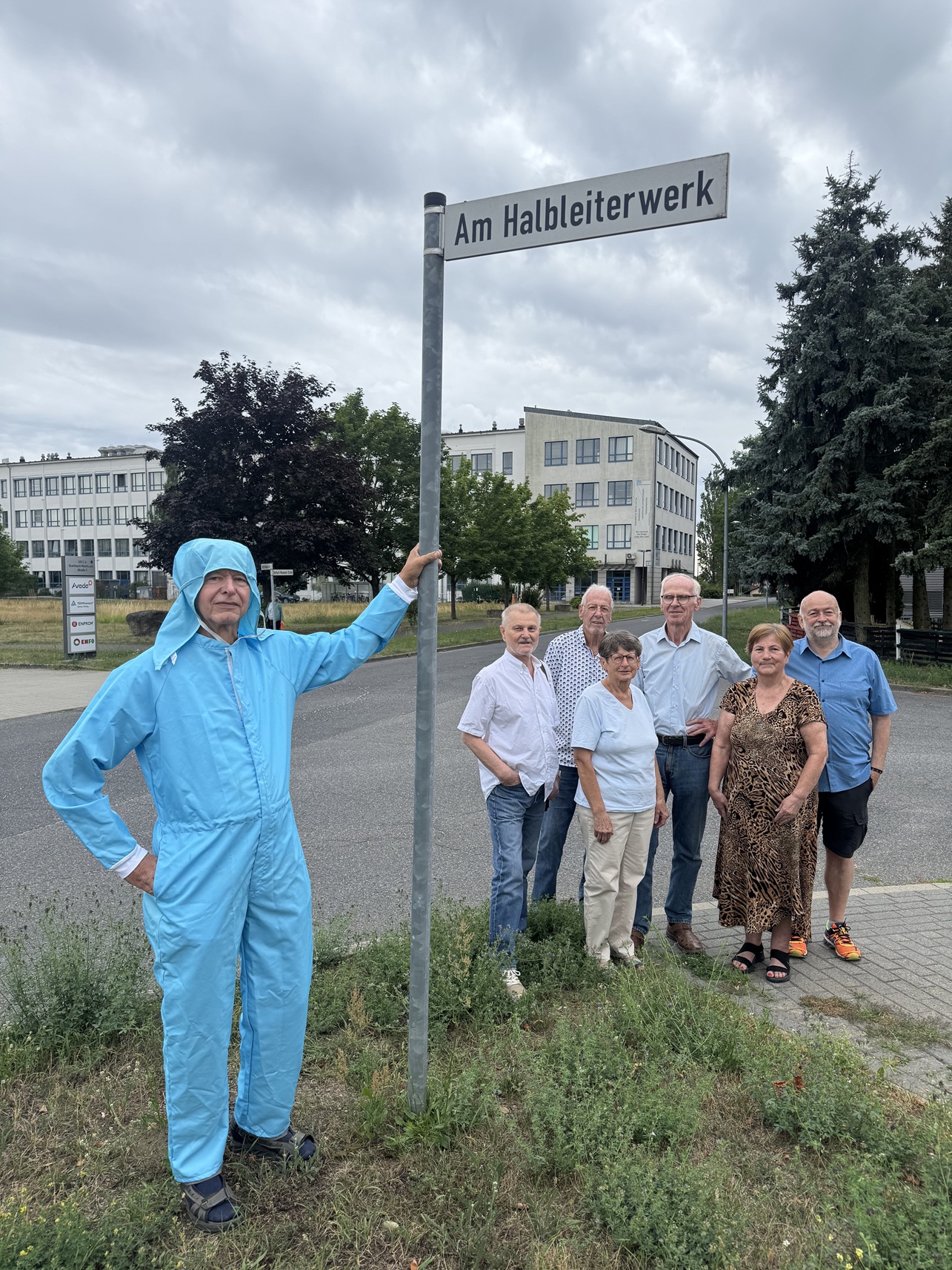Eine Gruppe Menschen steht neben einem Straßenschild "Am Halbleiterwerk"