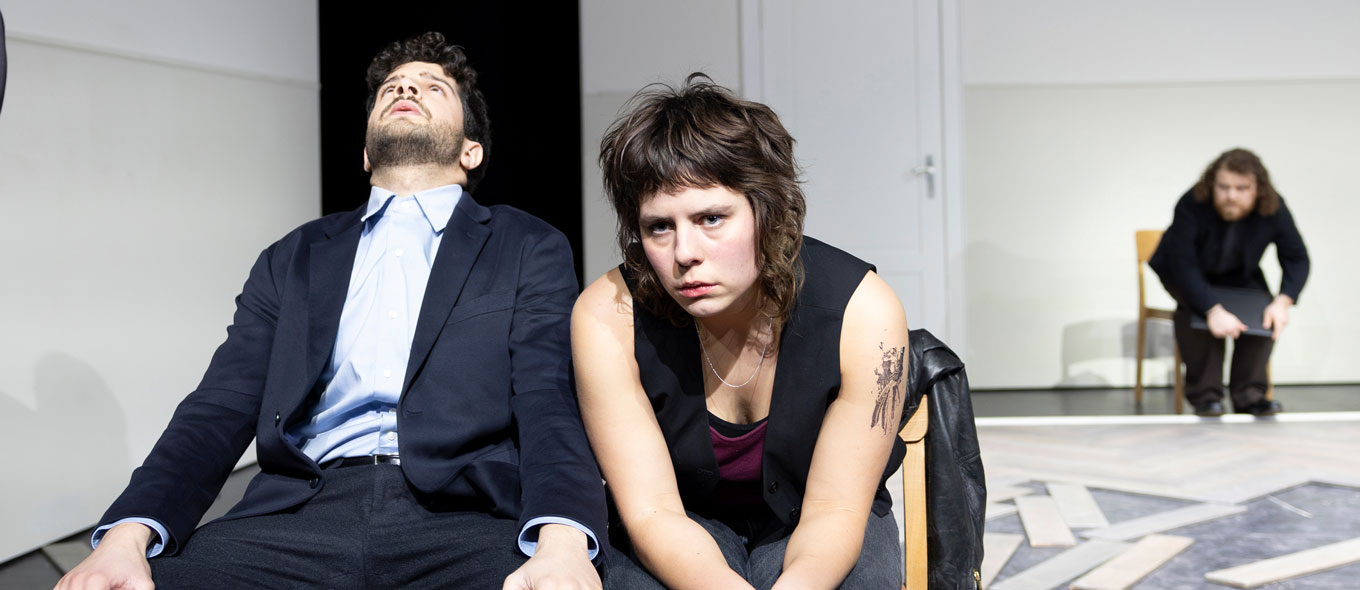 Szenenfoto aus dem Schauspiel "Aus dem Nichts": Eine Frau und ein Mann sitzen auf einer Bank. Sie sehen erschöpft und frustriert aus.